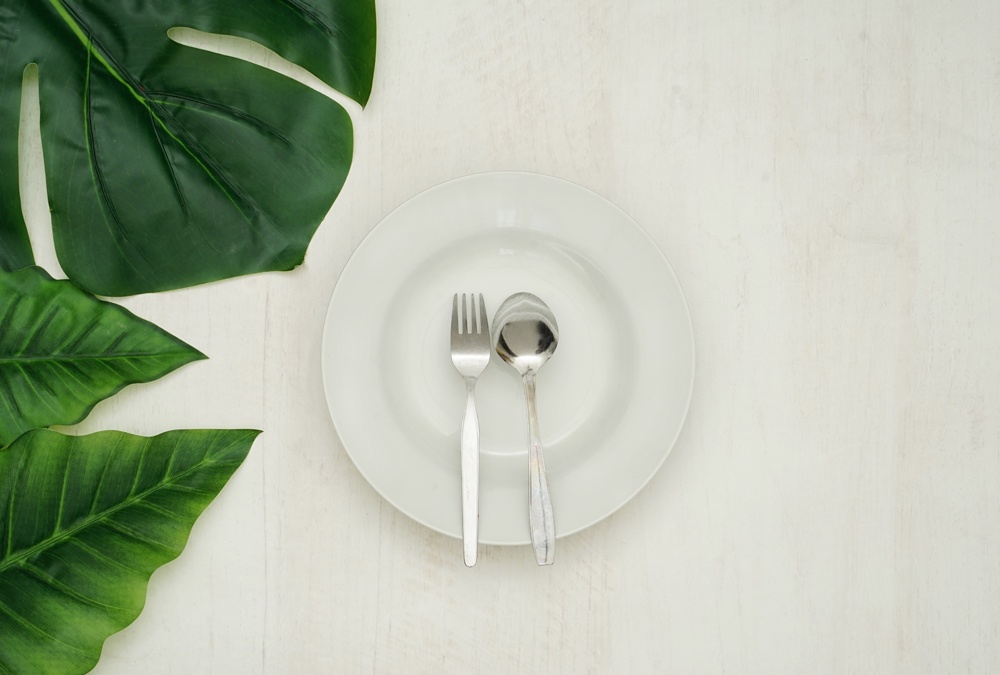 empty plate with fork and spoon on top with leaves on the side