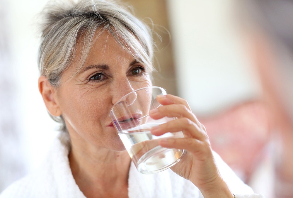 old lady with gray hair drinking a glass of water