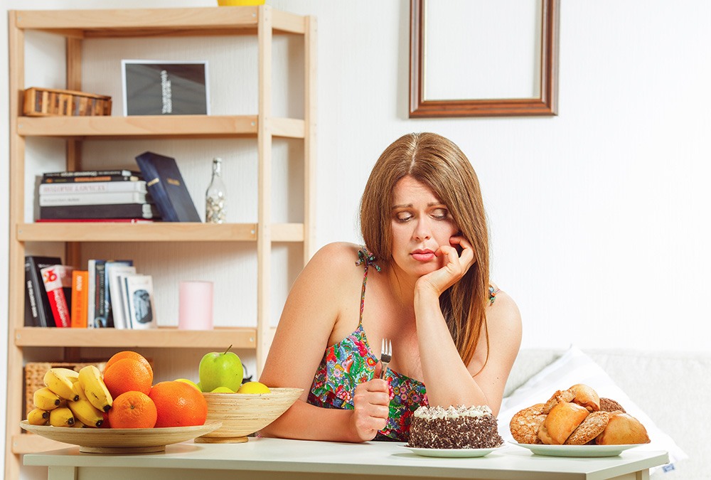 woman looking at cake and carbs all sad with fork in hand