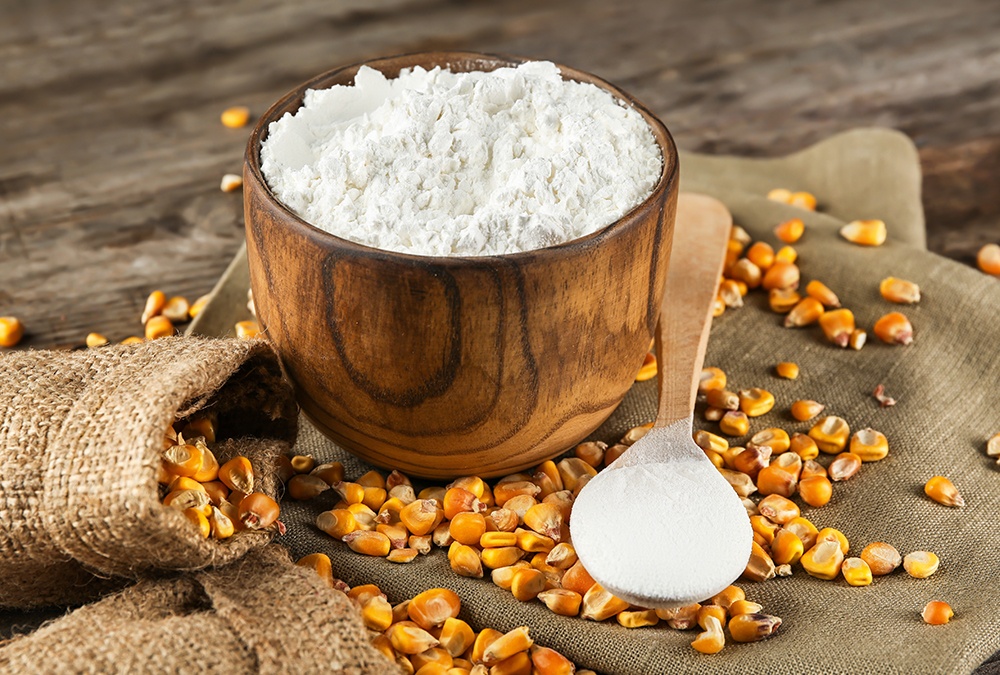 Wooden bowl of cornstarch and corn seeds on wooden table