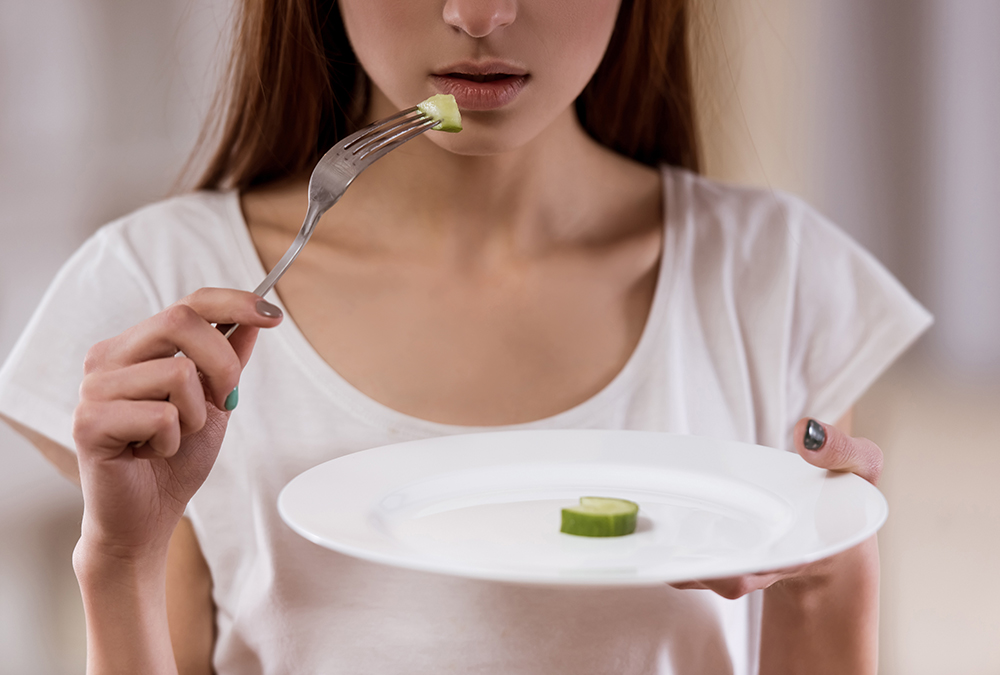 woman suffering from eating disorder eating one slice of cucumber on a plate