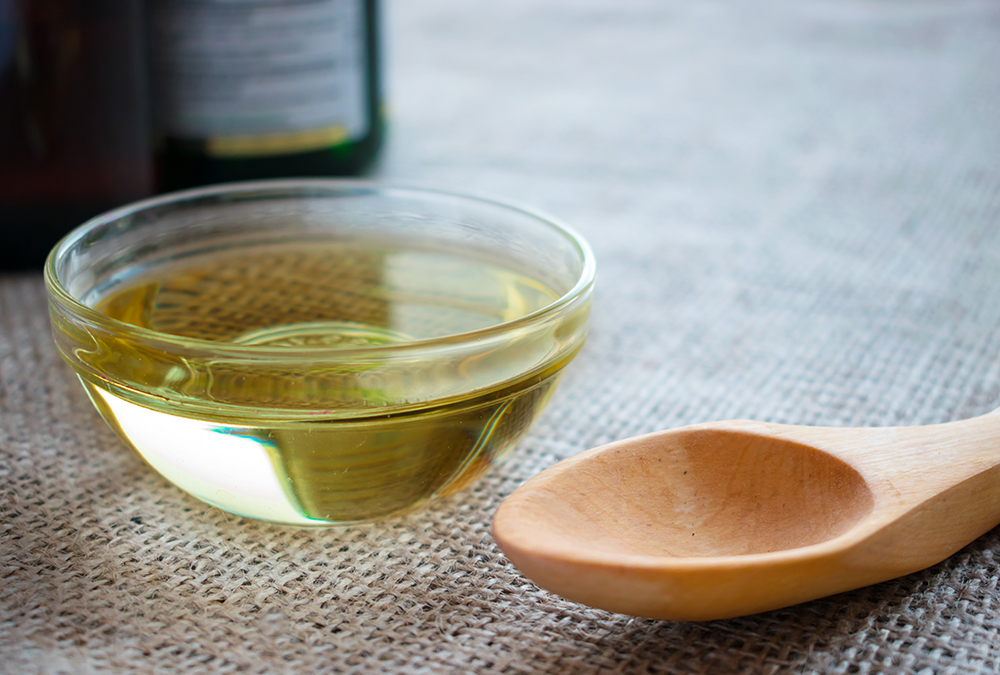 MCT oil in a clear bowl and a wooden spoon
