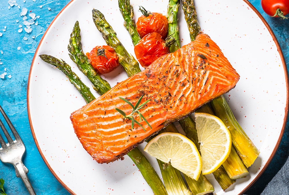 grilled salmon, tomatoes, asparagus lemon wedges on a white plate